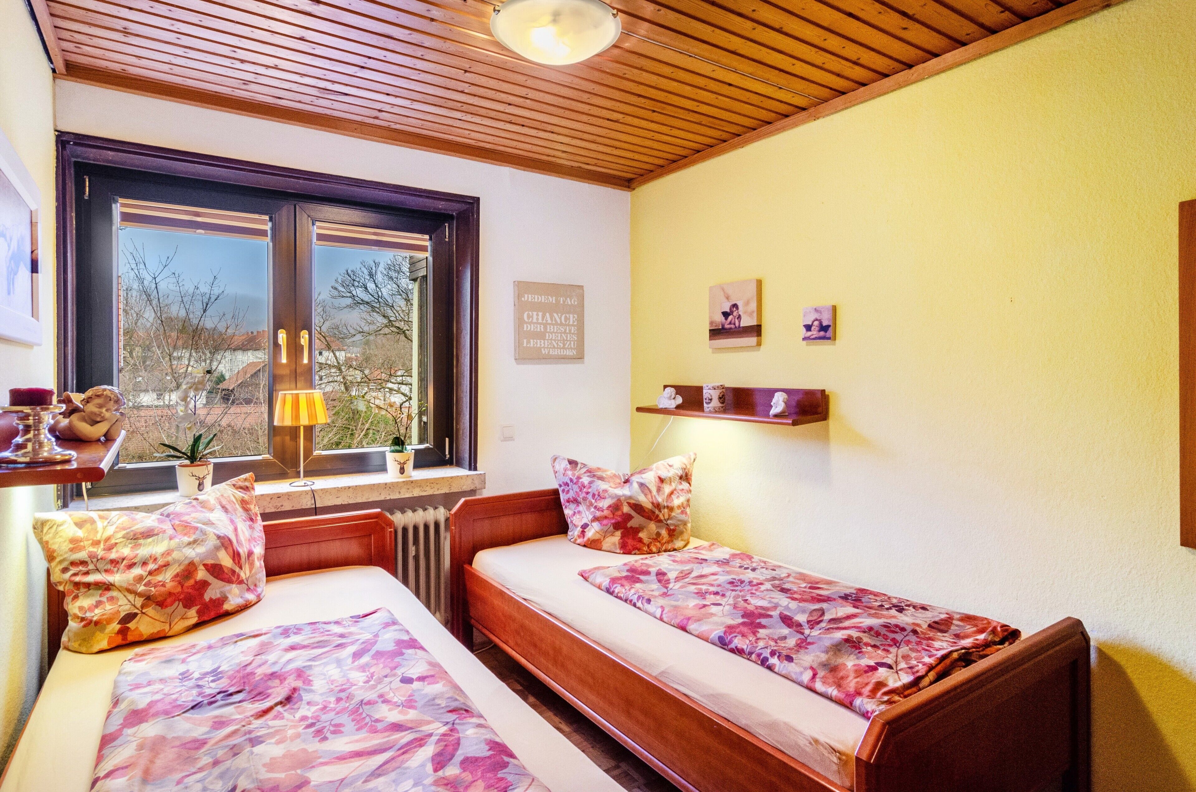 Een slaapkamer met twee bedden, een raam met uitzicht, een plank met spullen en een bord aan de muur.