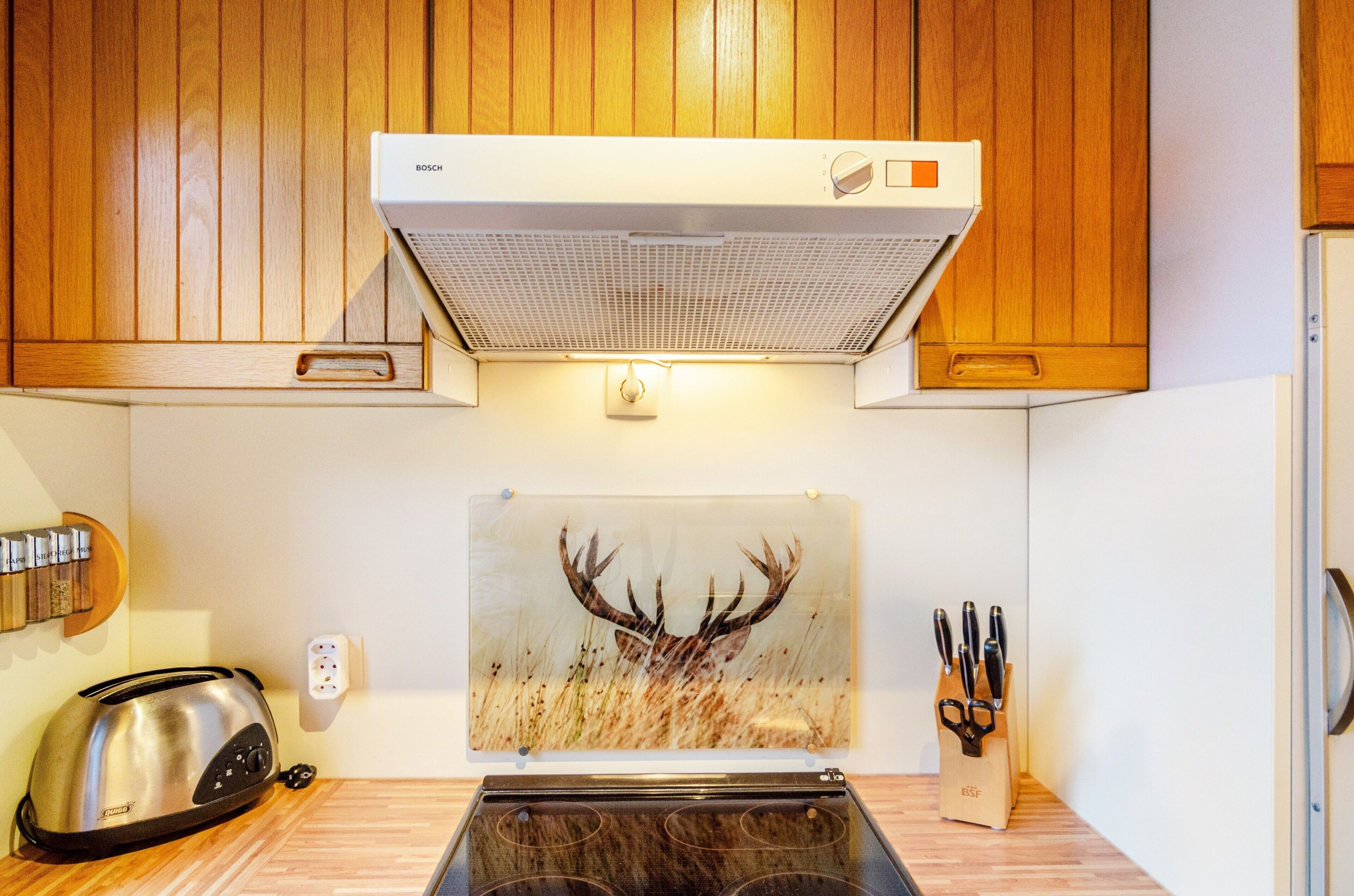 A kitchen with wooden cabinets, a Bosch range hood, a toaster, a knife block, and a deer antler artwork.