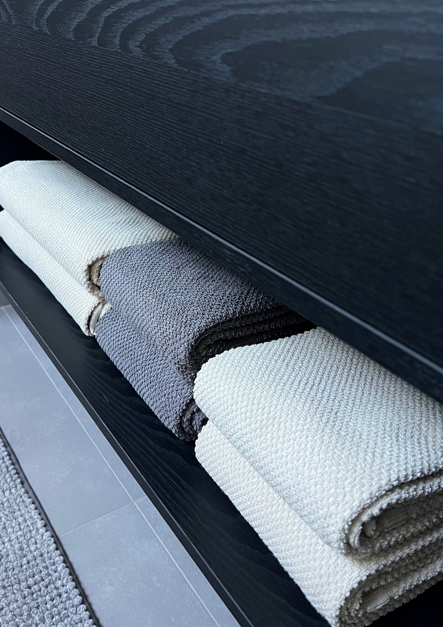 Une serviette grise et blanche, soigneusement pliée, est posée sur un banc en bois foncé.