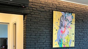 Ett modernt vardagsrum med en svart tegelvägg, en brun lädersoffa och en färgstark, abstrakt målning.