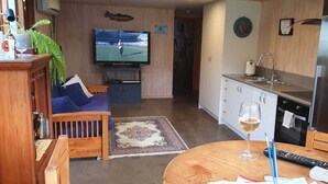 A compact living space with a sofa, TV, kitchen area, and a dining table with a glass of wine.