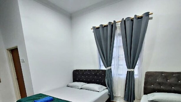 A hotel room with two beds, a ceiling fan, and a window with grey curtains.
