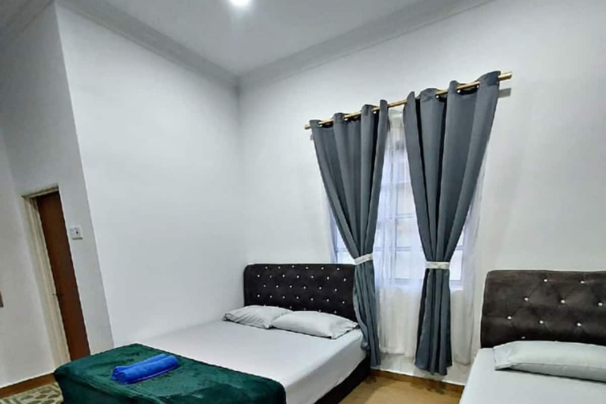 A hotel room with two beds, a ceiling fan, and a window with grey curtains.