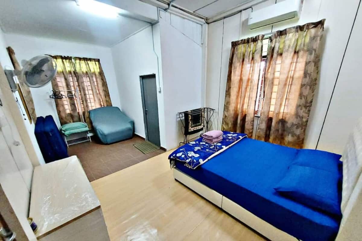 A compact room with a single bed, a chair, a small table, and a fan.
