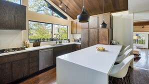 A modern kitchen with a large island, wooden cabinets, and a view of the outdoors. - 10-Acre Wellness Retreat, Pool, Sauna, Ceremony Tent | Fable Sonoma by AvantStay (Santa Rosa)