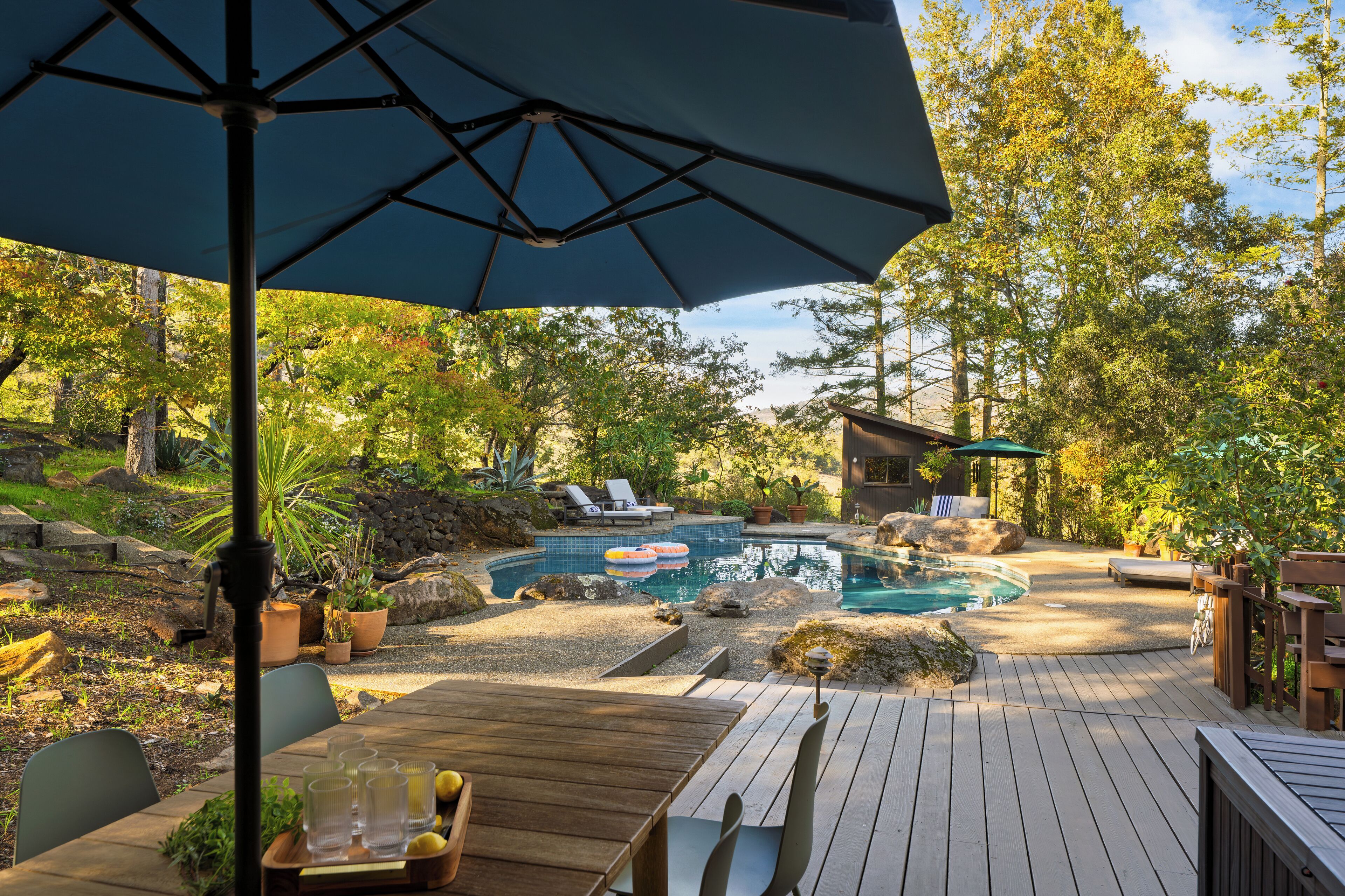 A wooden deck with a pool, lounge chairs, and an umbrella.