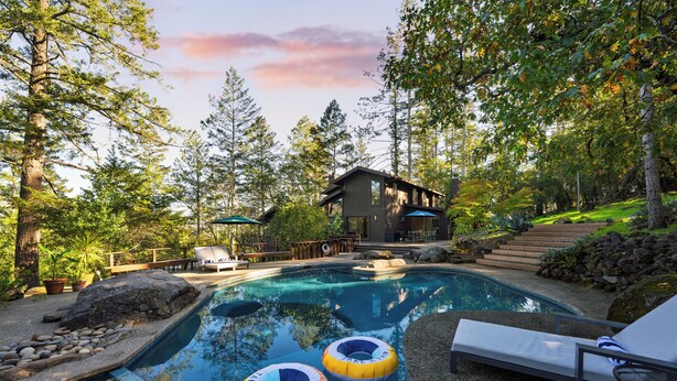 A swimming pool with lounge chairs and inflatable rings, surrounded by trees and a wooden cabin. - 10-Acre Wellness Retreat, Pool, Sauna, Ceremony Tent | Fable Sonoma by AvantStay (Santa Rosa)