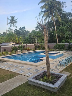 A rectangular swimming pool with a tiled deck, surrounded by a low wall and lush greenery, including palm trees and various plants. - Bliss Suites by SMS Hospitality (Panglao)