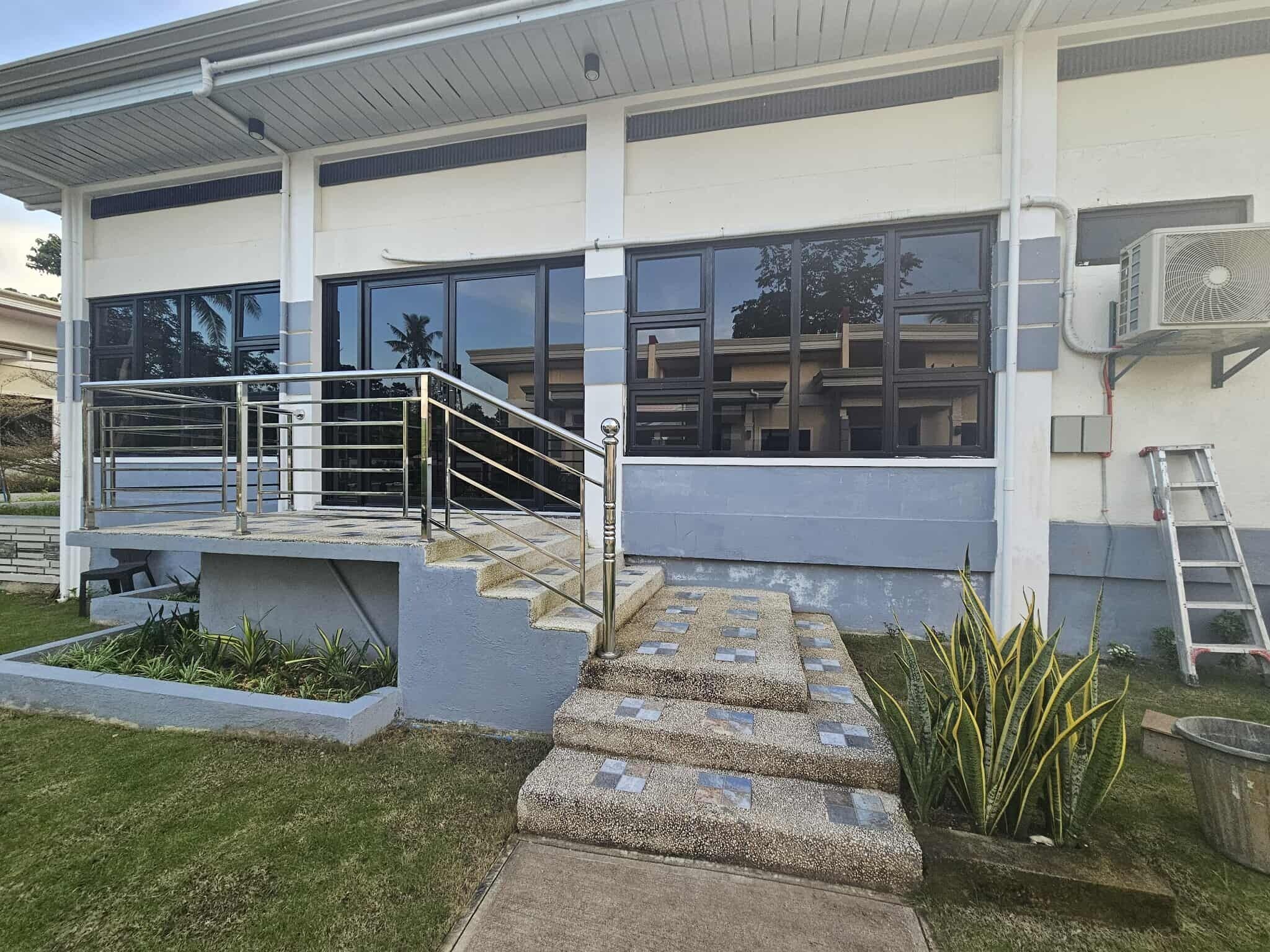 A modern building with a concrete staircase leading to a covered outdoor area, surrounded by a well-maintained lawn and plants.