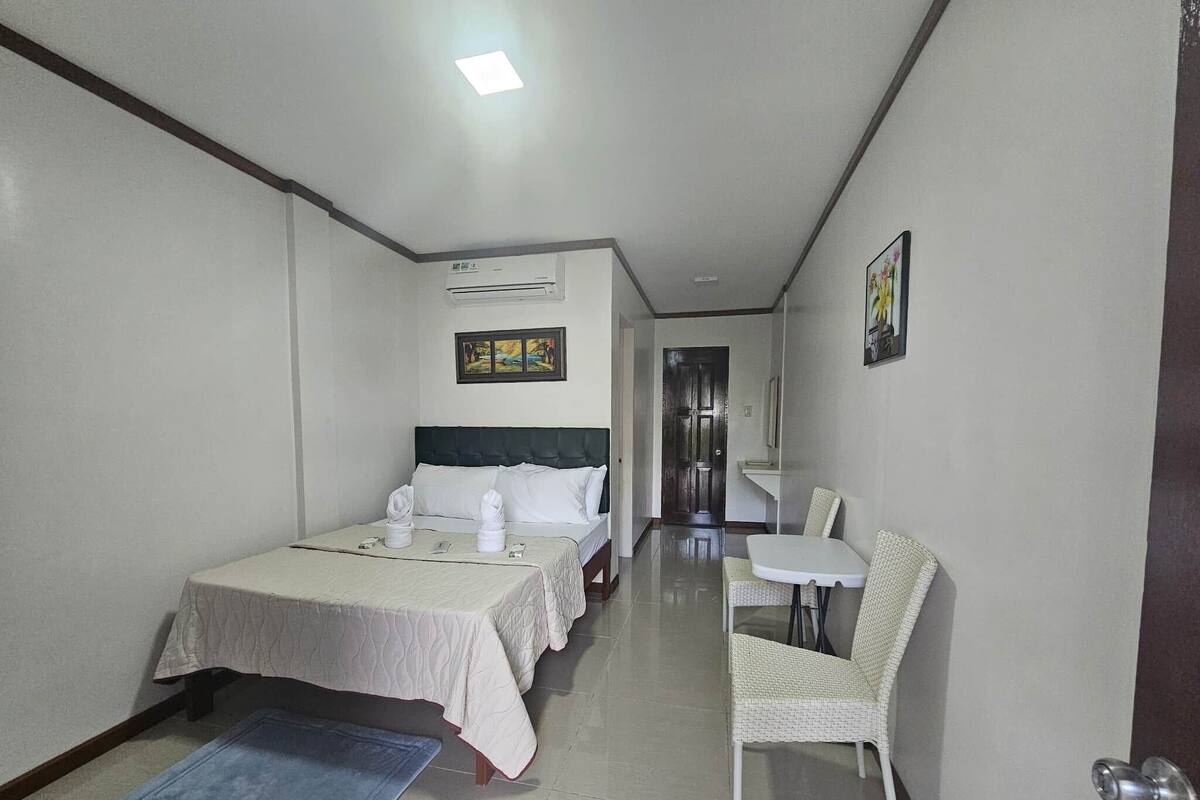 Une chambre d’hôtel avec deux lits, une petite table, une chaise et une salle de bain visible à travers une porte ouverte.