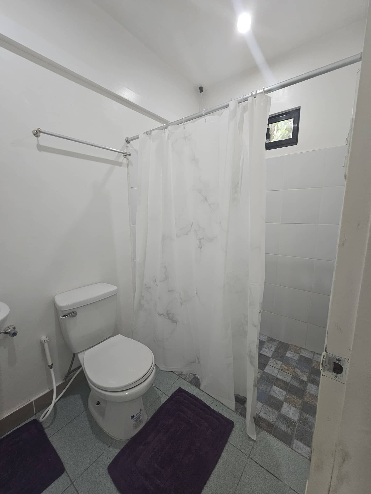 Un baño pequeño con inodoro, cortina de ducha y piso de baldosas.