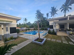 A residential area with a swimming pool, palm trees, and a covered patio area. - Bliss Suites by SMS Hospitality (Panglao)