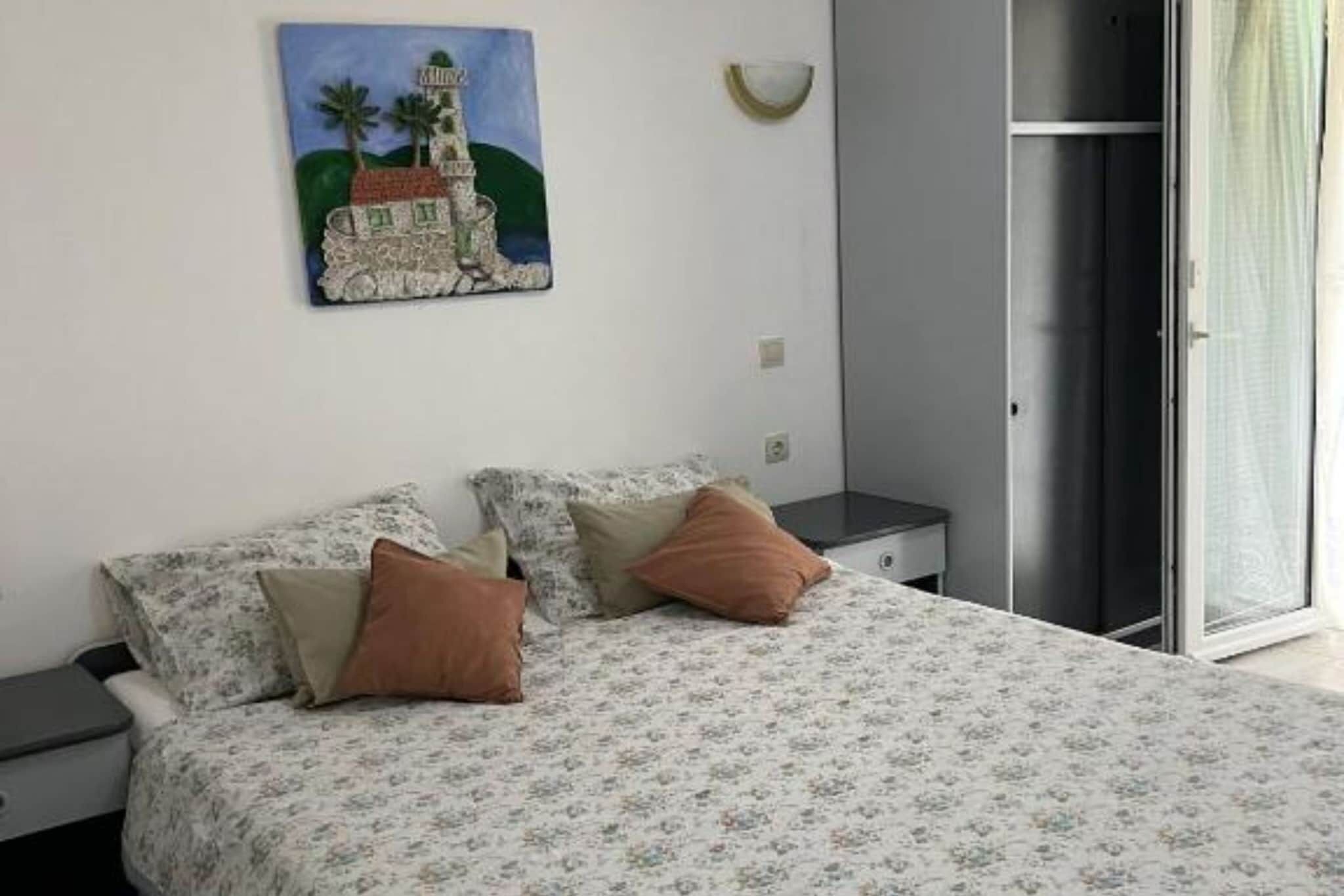 A bedroom with a bed, pillows, a nightstand, a painting, and a sliding door.