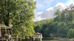 A riverside park with a gazebo, a small building, and a stone pathway leading to the water. - Waldhotel Silbermühle (Horn-Bad Meinberg)