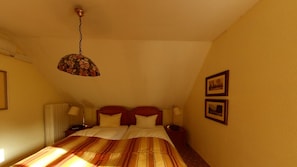 A bedroom with a bed, two bedside lamps, a hanging light fixture, and two framed pictures on the wall.