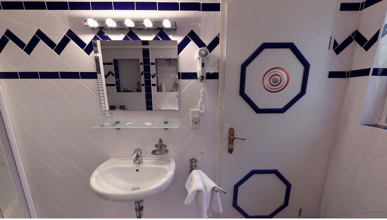 Un baño con lavamanos blanco, espejo y perchero.