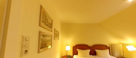A hotel room with a bed, bedside lamps, a nightstand, and wall-mounted artwork.
