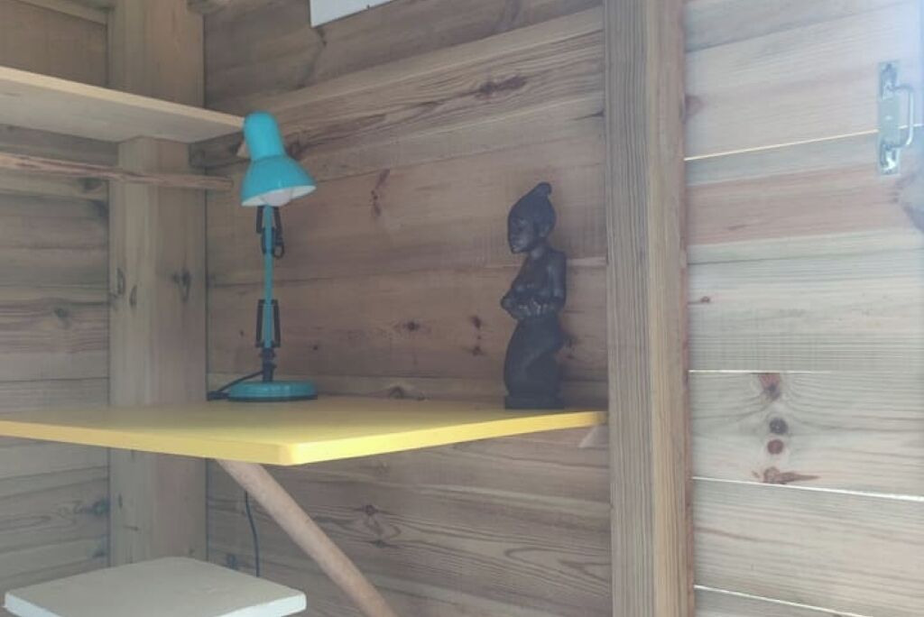 Um interior de madeira com uma prateleira amarela, uma luminária de mesa azul e uma pequena estátua.