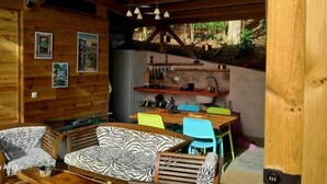 Une cabane en bois comprenant un coin repas, une cuisine et un espace détente avec des coussins à motifs zébrés.