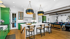 A modern kitchen with a central island, green cabinetry, and hanging pendant lights.