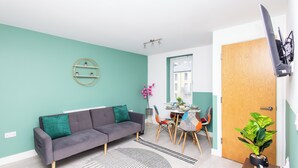 Ein modernes Wohnzimmer mit grauem Sofa, türkisfarbenen Wänden, einem Essbereich mit Tisch und Stühlen und einer Holztür.