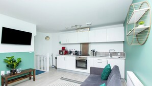 Eine moderne Küche mit weißen Schränken, einem eingebauten Ofen und einer Mikrowelle. Im Wohnbereich befindet sich ein graues Sofa mit türkisfarbenen Kissen.