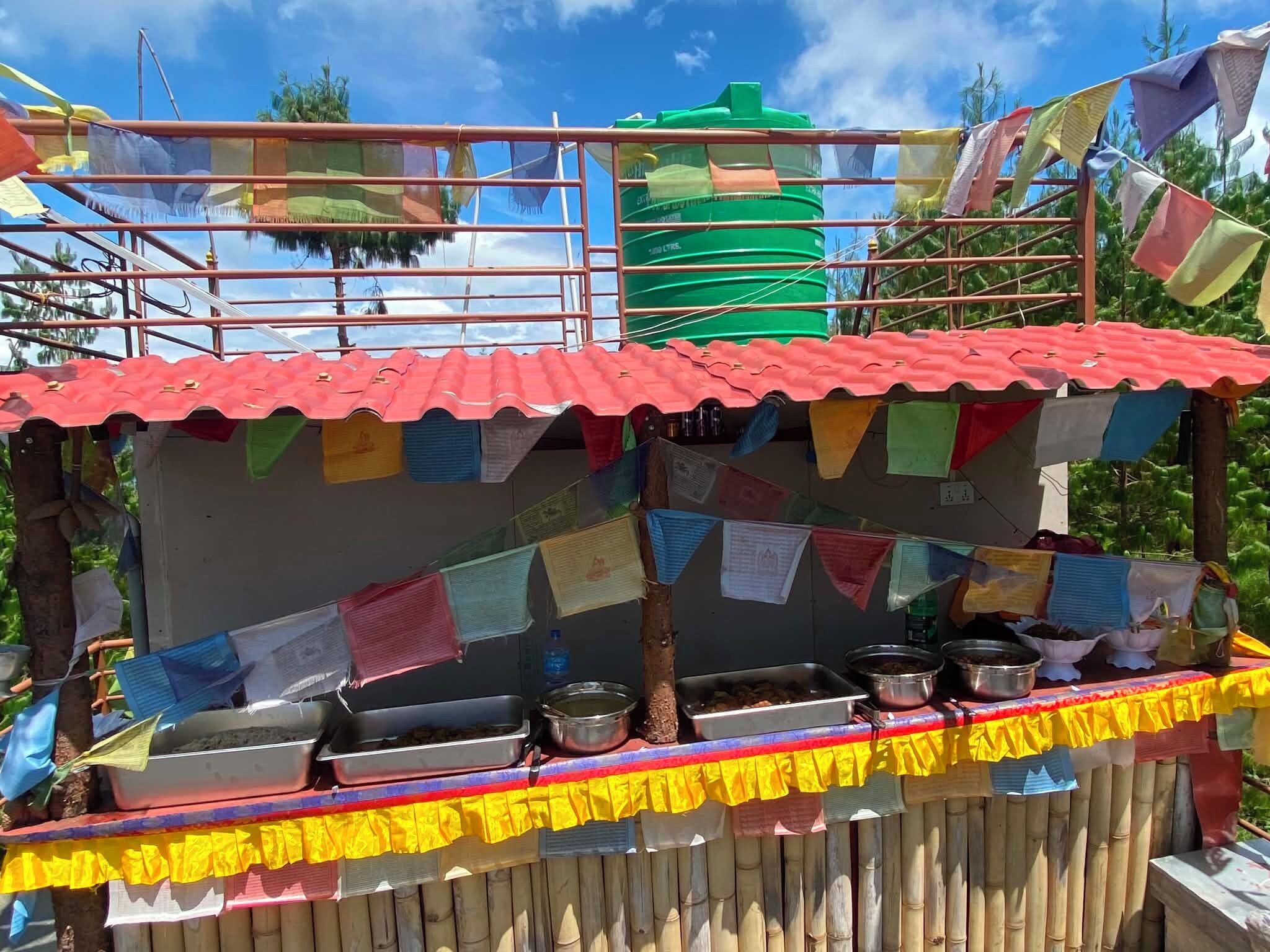 A food stall with a red roof, various cooking utensils, and colorful prayer flags.