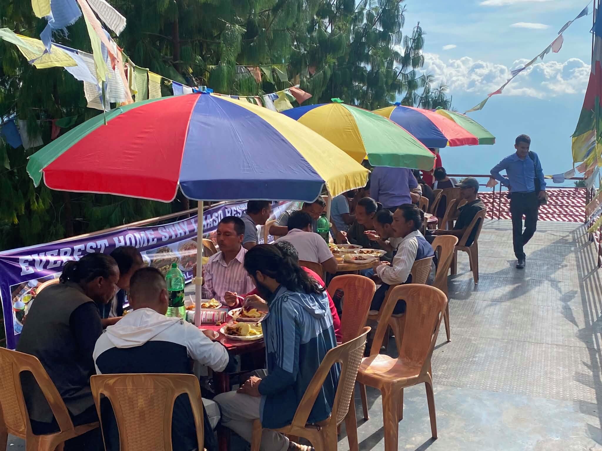 Un groupe de personnes déjeunant ou dînant sous des parasols colorés lors d’un événement en plein air.