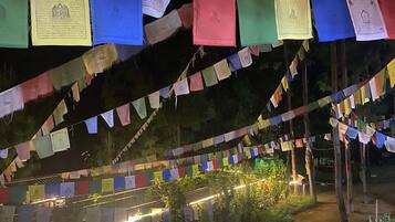 Ein Pfad, gesäumt von Grün und beleuchtet durch künstliche Lichter, mit bunten Gebetsfahnen, die darüber gespannt sind.