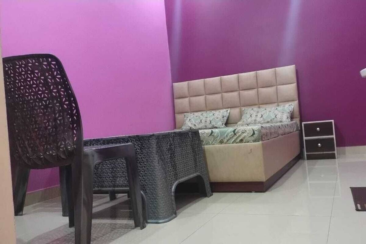 A bedroom with a bed, a chair, a small table, a sink, and a trash bin.