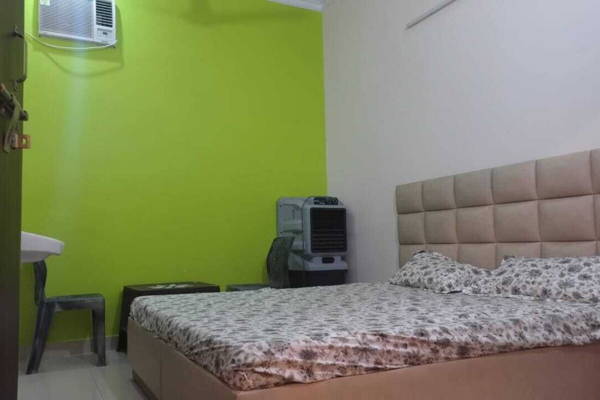 A bedroom with a bed, a bedside table, a chair, a radiator, and a wall-mounted air conditioner.