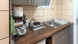 A compact kitchenette with a sink, a small refrigerator, and a stove. - Meli Studio 304 – Comfort & Functionality for up to 4 Guest (Paralia)