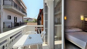 A balcony with a table and chairs, a bed, and a view of neighboring buildings. - Meli Studio 304 – Comfort & Functionality for up to 4 Guest (Paralia)