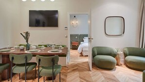 A modern living room with green upholstered chairs, a dining area with a wooden table set for four, a flat-screen TV mounted on the wall, and a large mirror on the wall. - Sublime apartment in the center of Paris (Paris)