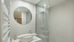 Ein modernes Badezimmer mit rundem Spiegel, weißen Fliesen und einer Glasdusche.