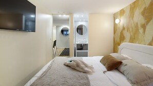 Ein Hotelzimmer mit Bett, Wandfernseher, Badezimmer mit Spiegel und Waschbecken sowie einer Wand mit Muster.