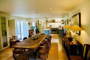 A spacious dining area with a large wooden table, surrounded by chairs, and a kitchen in the background. - Cotswold Country House in Charlbury (Charlbury)