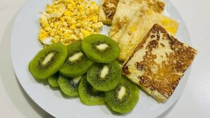 Un plato con huevos revueltos, tostadas y kiwi en rodajas.