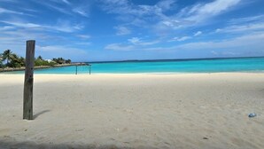Una playa con agua turquesa cristalina, un poste de madera y una red de voleibol.