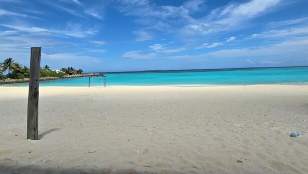 A beach with clear turquoise water, a wooden post, and a volleyball net. - Gorgeous 7-bedroom house with AC in peaceful Shaviyani Atoll Milandhoo, Maldives (Milandhoo)