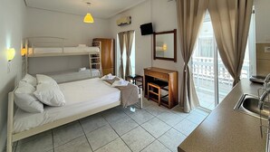 Quarto de hotel com beliches, escrivaninha, espelho, televisão e varanda com cortinas.
