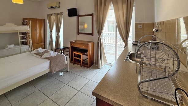 Quarto de hotel com beliche, escrivaninha, mesinha, pia e varanda com cortinas.