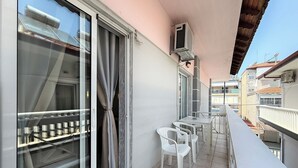 Uma varanda com porta de correr de vidro, uma mesinha com cadeiras e um ar condicionado montado no teto.