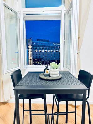 A dining area with a table and chairs, a window with a view of a building labeled "WIMBERT," and a small potted plant on the table. - Elegant 4BR Apt Near Westbahnhof (Vienna)