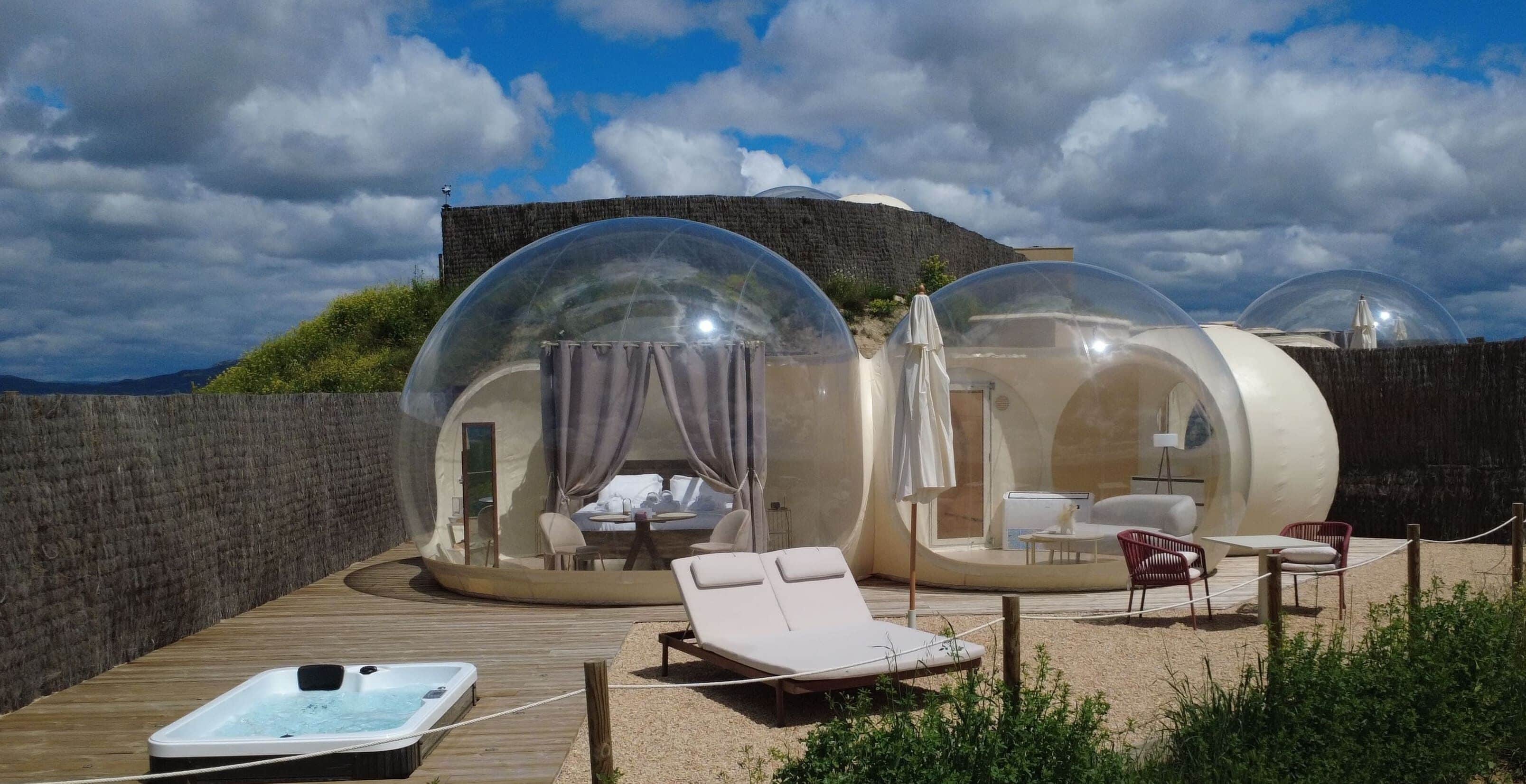 Alojamiento con forma de cúpula transparente, que incluye una bañera de hidromasaje, sillones de descanso y una terraza de madera.