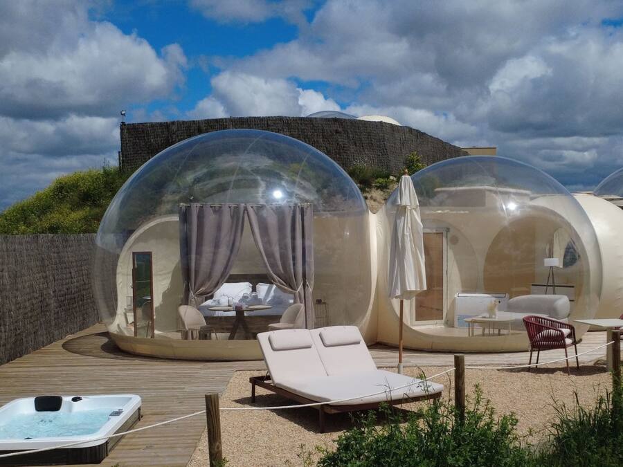 Alojamiento con forma de cúpula transparente, que incluye una bañera de hidromasaje, sillones de descanso y una terraza de madera.