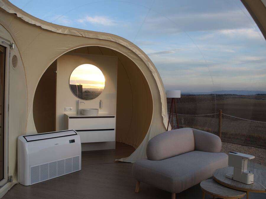 A tent-like room with a round mirror, a sink, a chair, and a table.