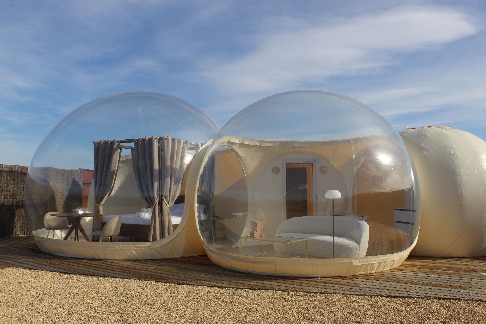 Dos estructuras esféricas transparentes con mobiliario interior, incluyendo un sofá y una mesa, sobre una superficie de grava.