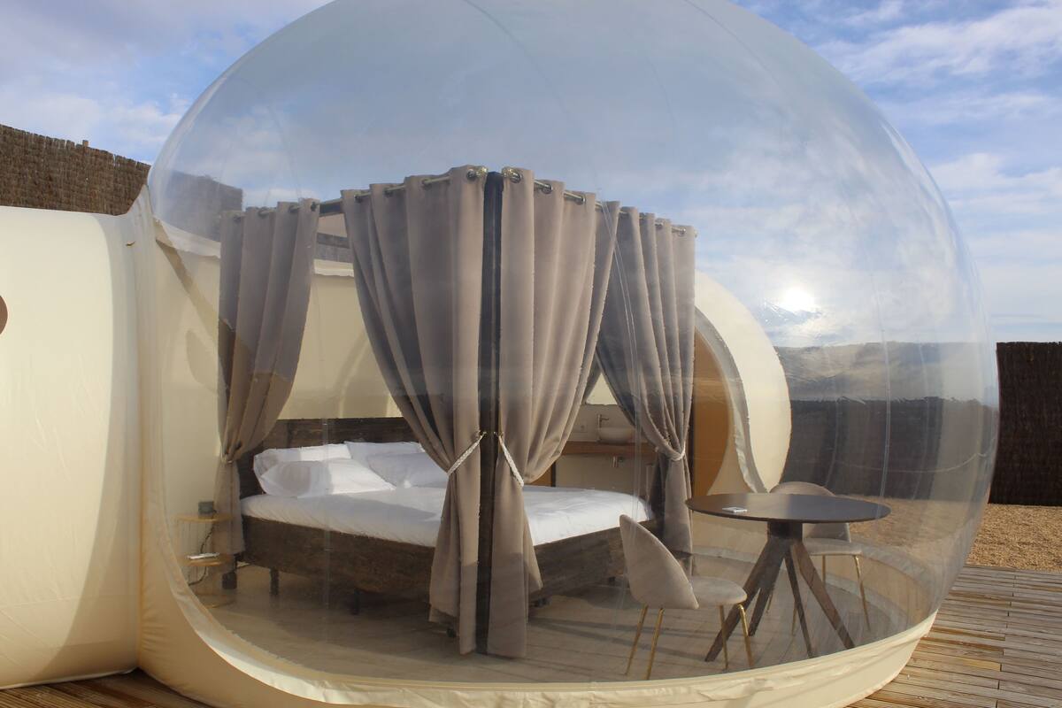 A transparent dome room with a bed and a small table.