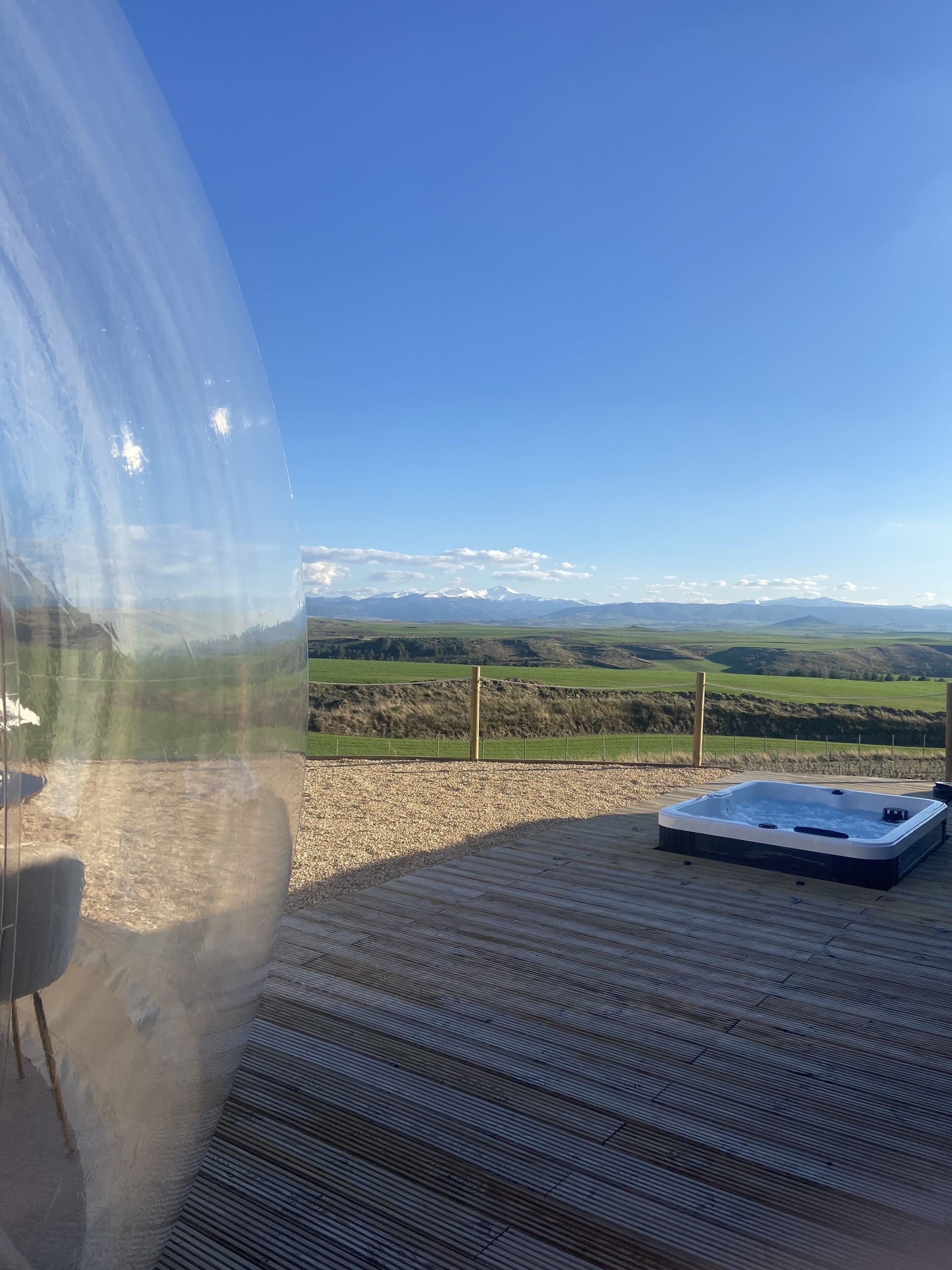 Un jacuzzi en una terraza de madera con vistas despejadas a un paisaje montañoso.